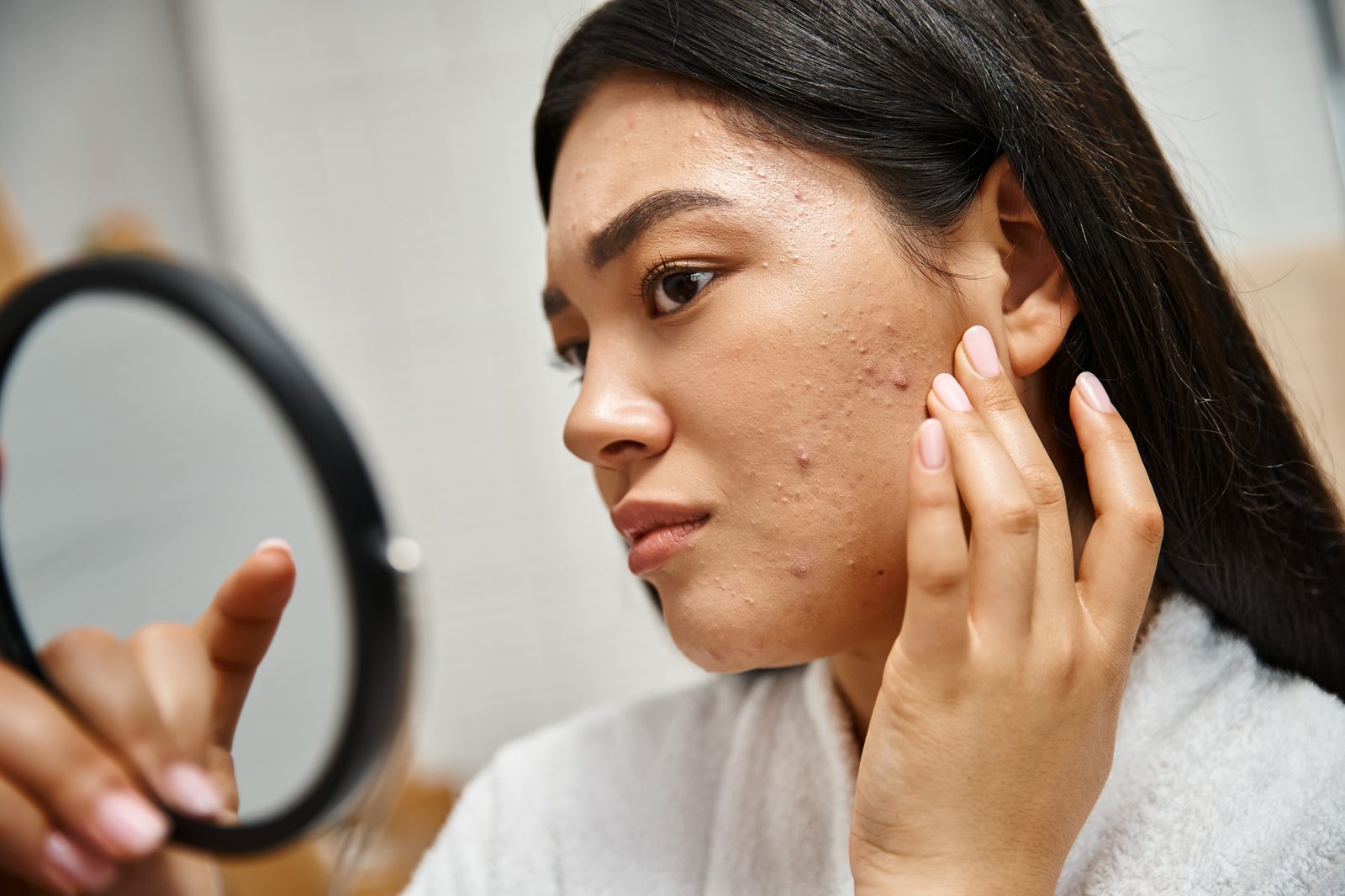 Young woman checking a breakout on her cheek in a hand mirror