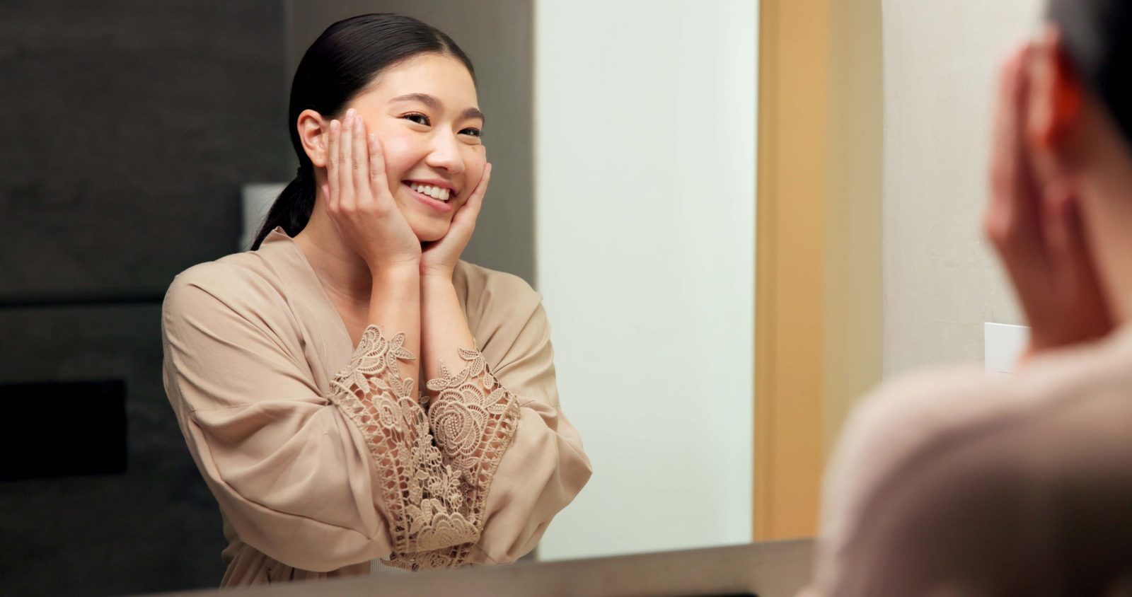 Smiling young woman admiring her skin in a bathroom mirror