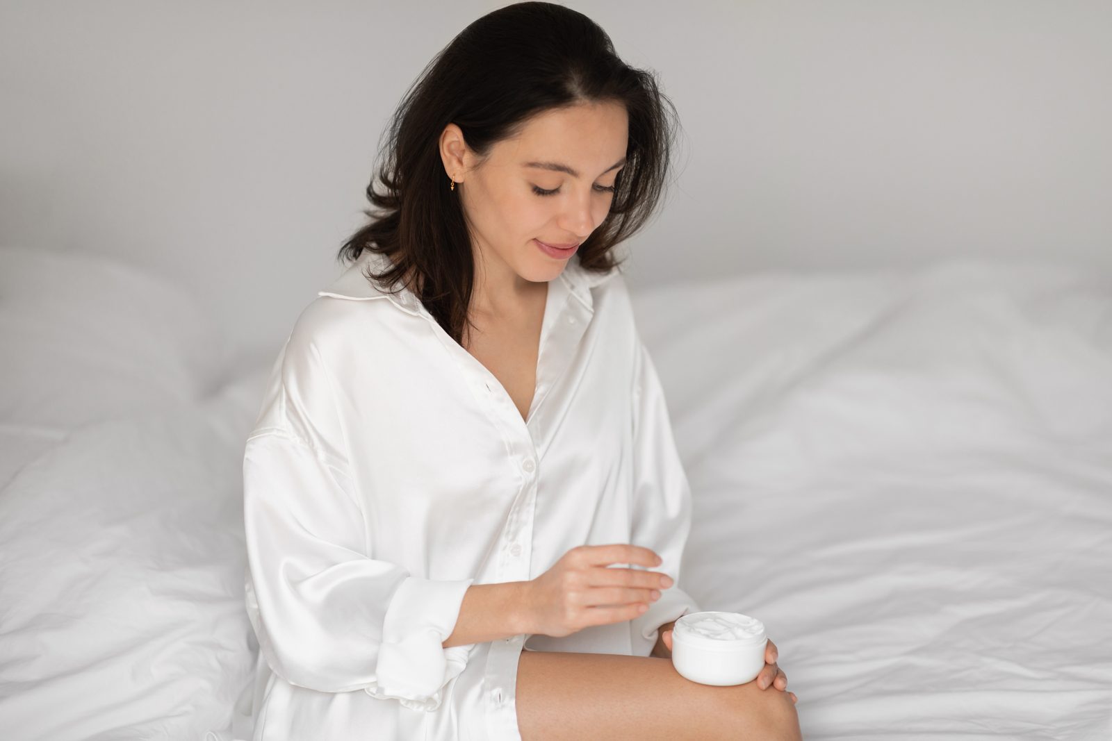 Woman in sleepwear applying face cream in her bedroom