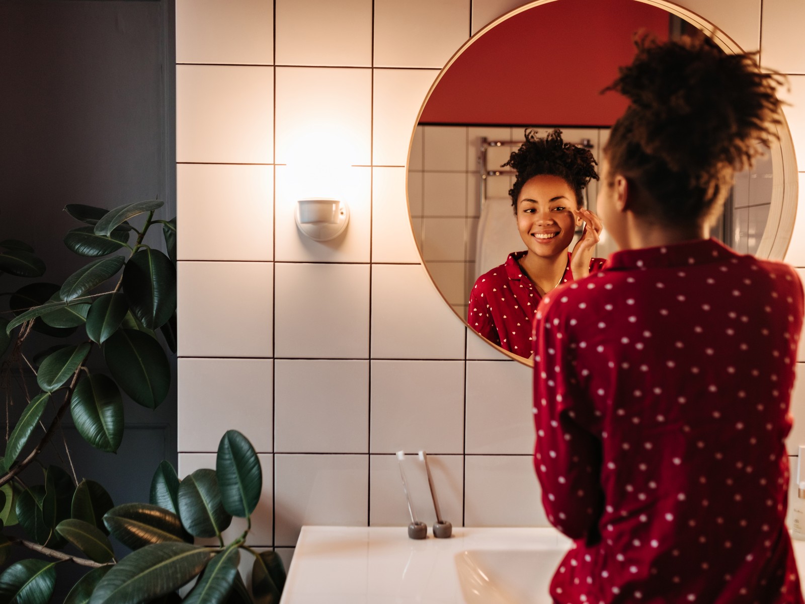 Woman in pyjamas smiling at her reflection in a round bathroom mirror