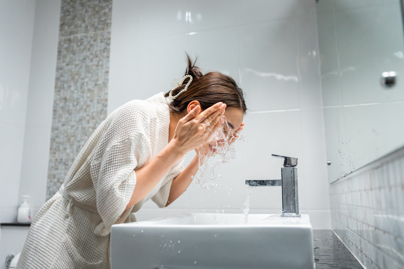 Woman in a white robe washing her face in the bathroom
